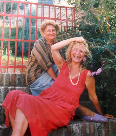 Fotografia a colori: due donne sedute su una scala all'aperto, una con un vestito rosso.