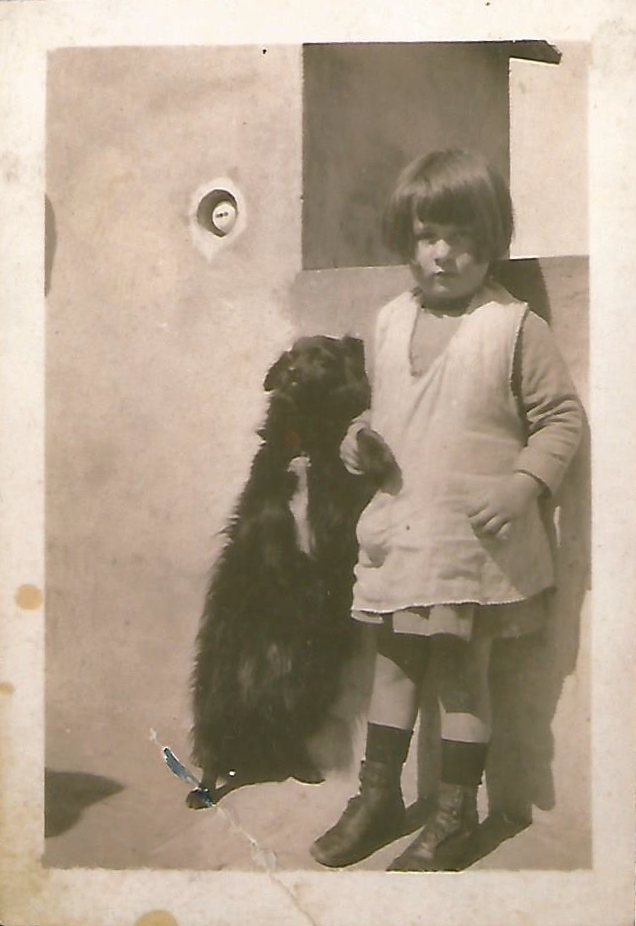 Fotografia d'epoca: la madre Lina bambina, in piedi accanto a un cane nero.